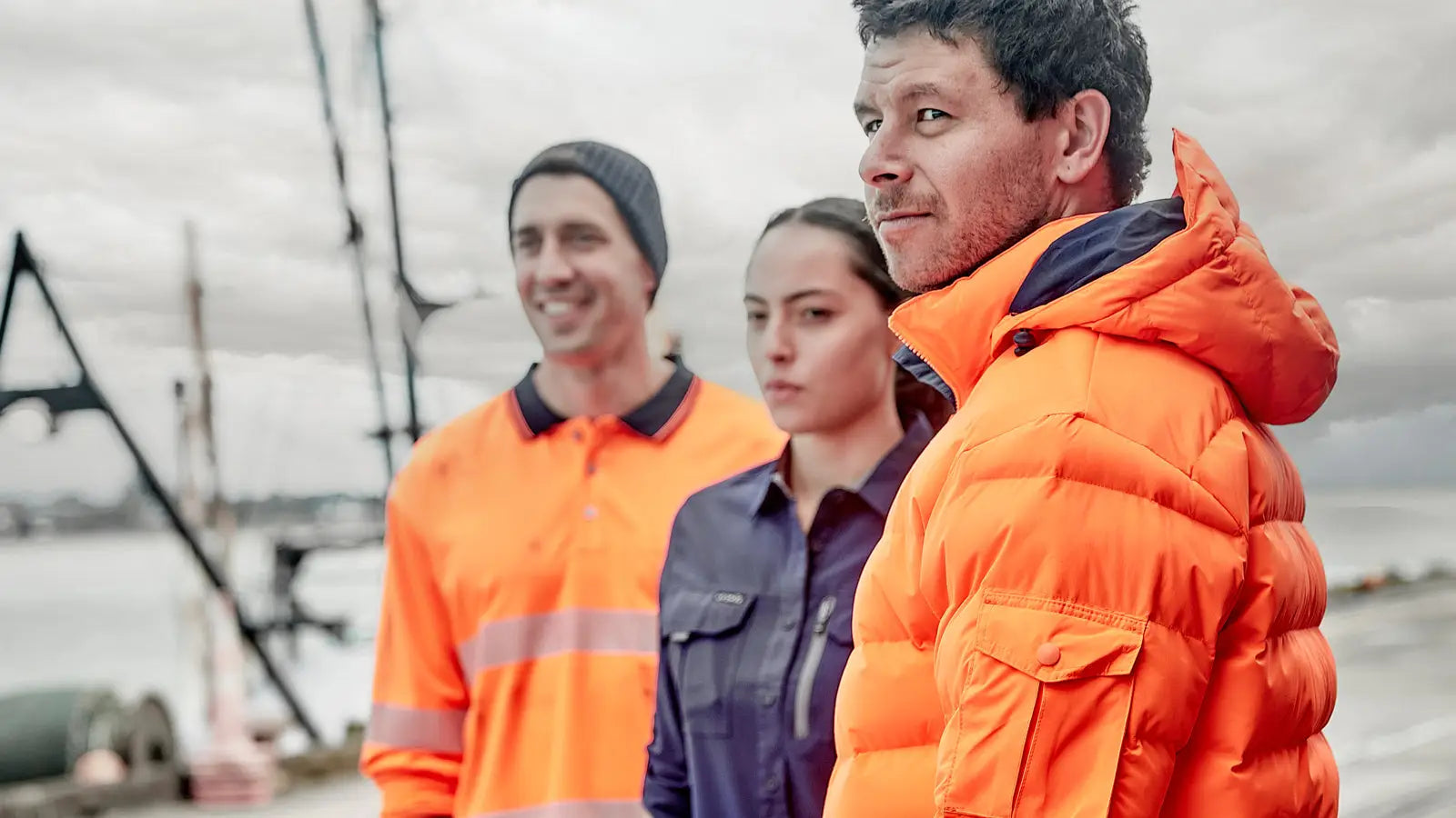 Three workers in safety clothing, one in bright orange work wear, outdoors