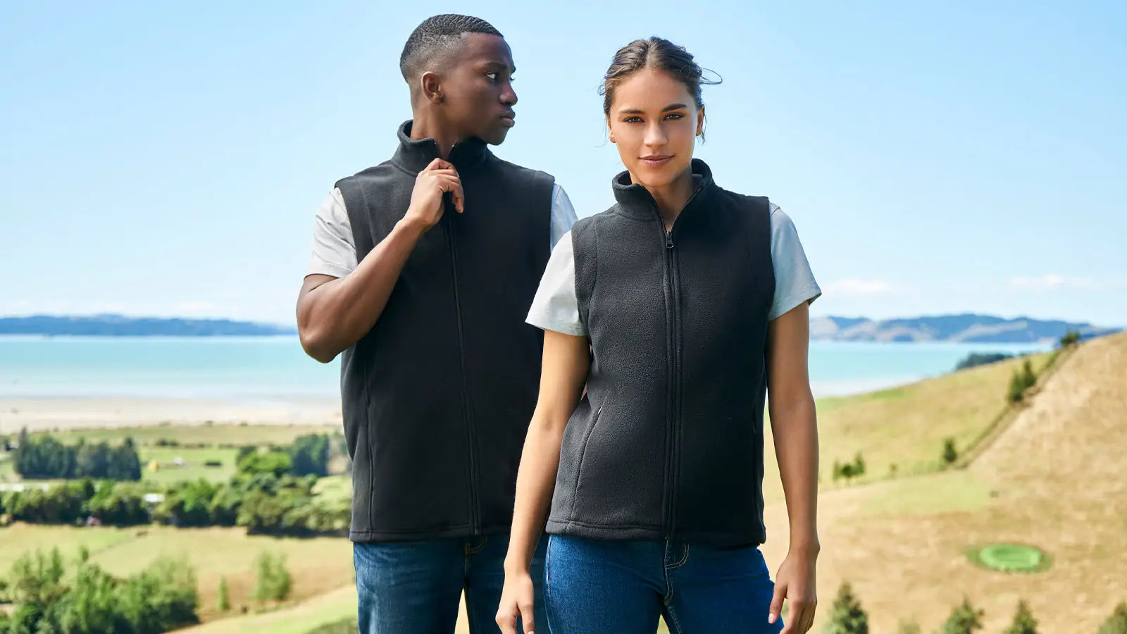 Two people modeling black fleece vests at Uniform Super Store in a casual setting