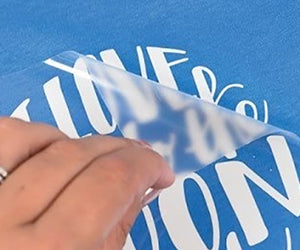 Clear transfer film peeling from blue fabric showing white lettering for single colour prints