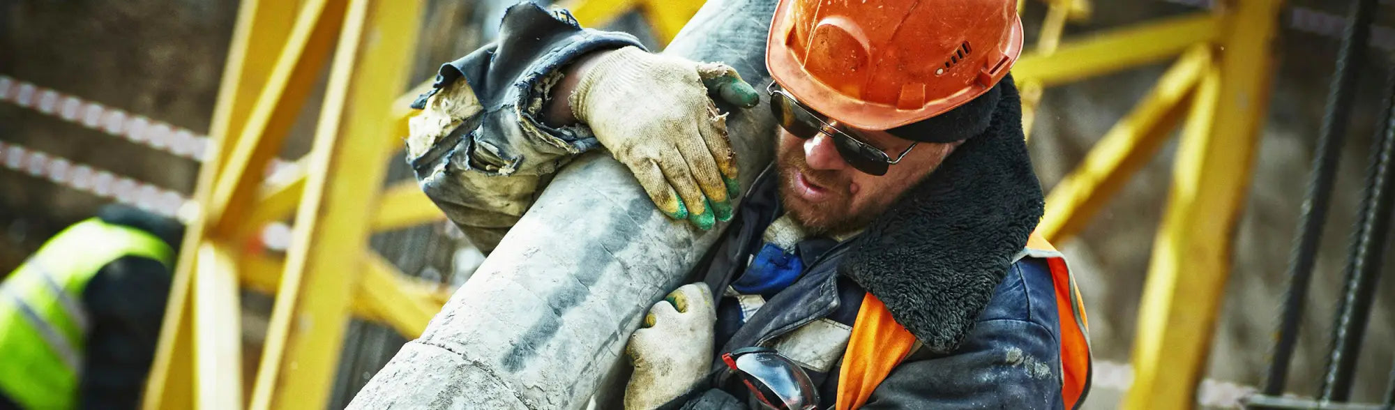 Construction worker carrying pipe in PPE Sun Protection collection showing sun safety gear