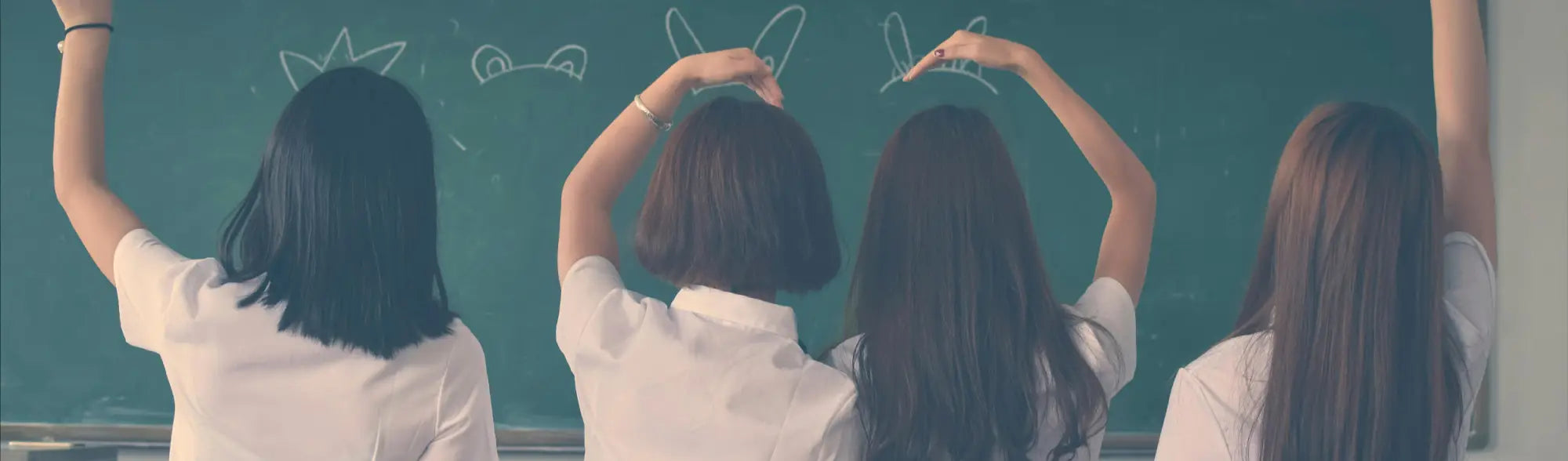 Four girls in school uniforms drawing on a chalkboard for School Shirts collection