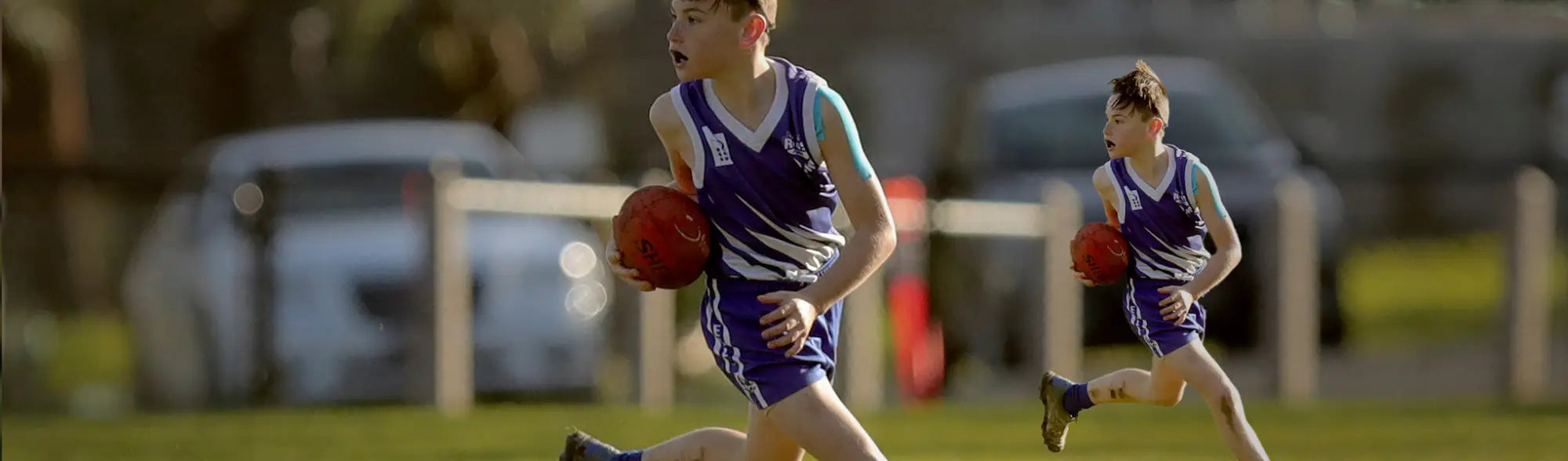 Two boys in Aussie Rules sportswear playing Australian Rules Football outdoors