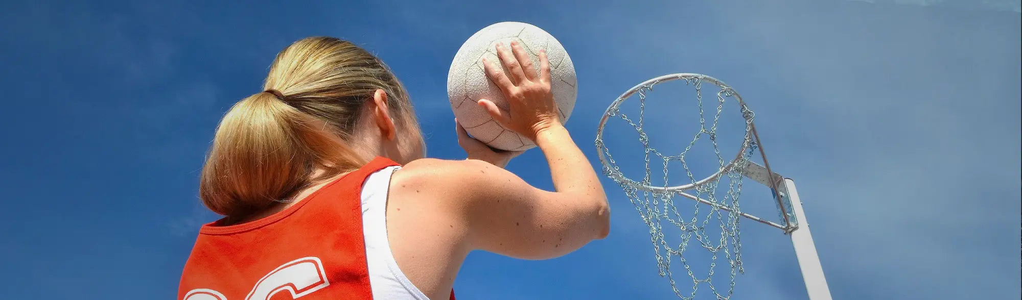 Netball player shooting in action wearing stylish netball teamwear and uniforms
