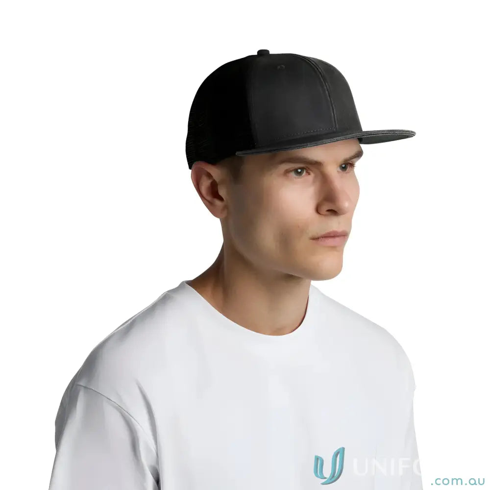 Person wearing AS Colour Faded Trucker Cap with black flat-brim and white tee