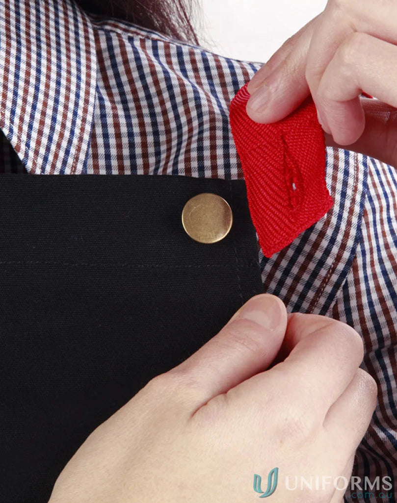 Person attaching red fabric to black Brunswick Bib Apron, stylish functional workwear