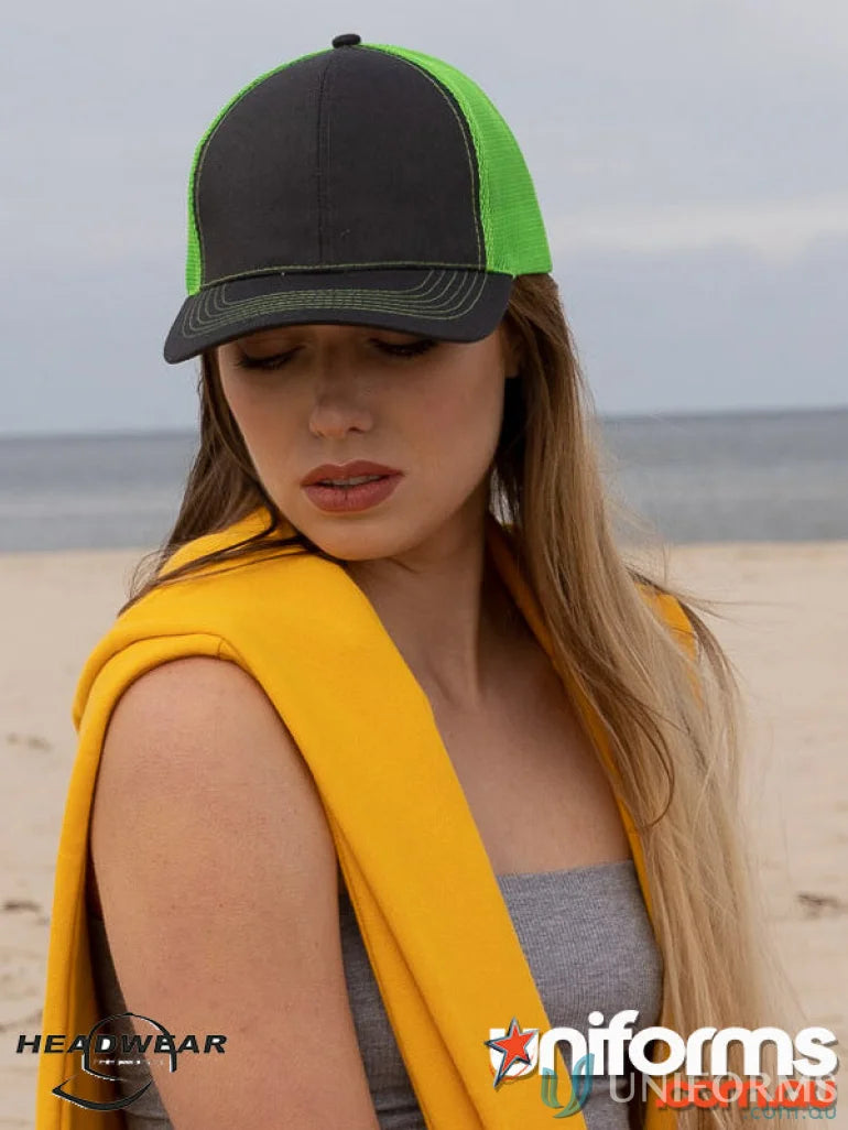Young woman wearing black and neon green trucker hat and yellow sweatshirt, perfect for workwear or uniforms