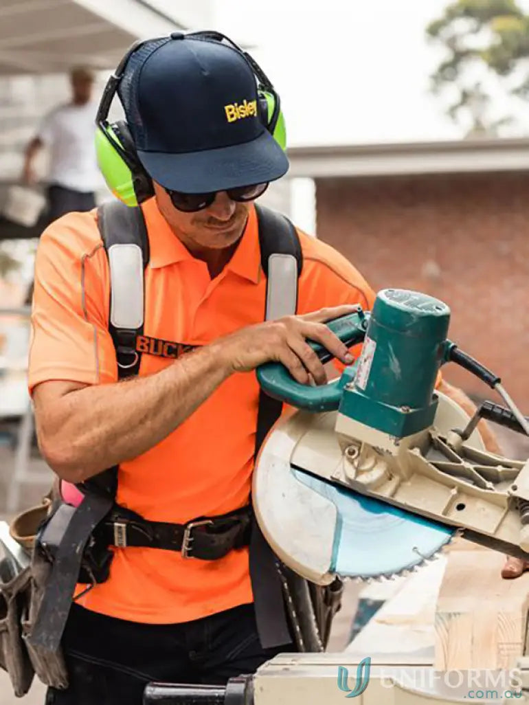 Construction worker in safety gear using a miter saw wearing a cool mesh polo with reflective piping