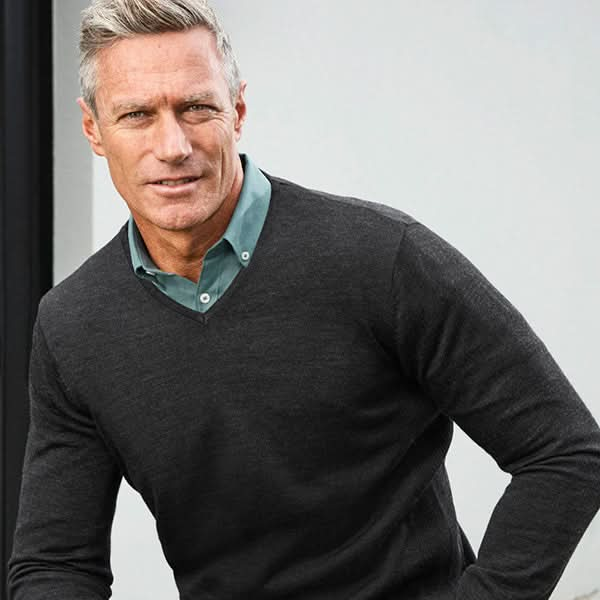 Man wearing a dark gray sweater over a green shirt against a light background