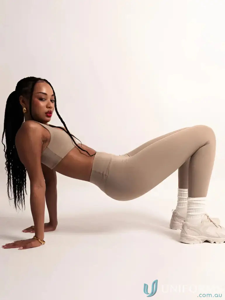 Woman in beige athletic wear showing Invicible Scrunch Latte Leggings for workout uniforms