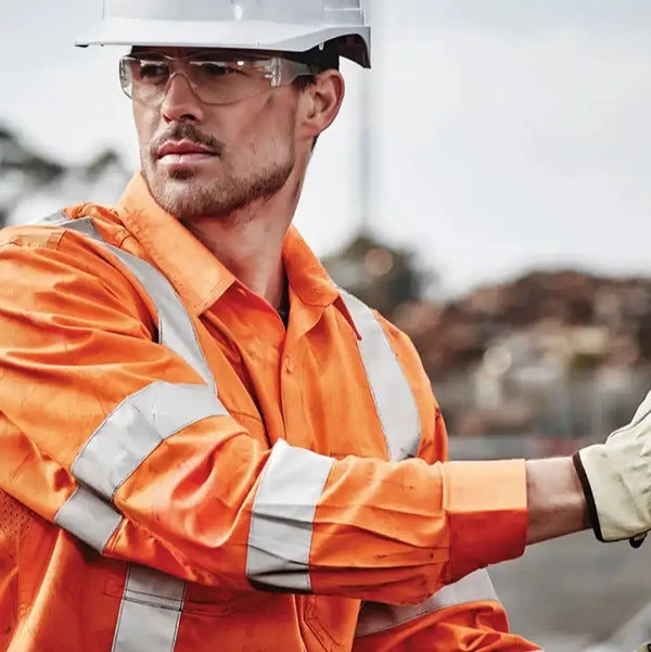 Person wearing an orange safety suit and white hard hat with reflective stripes, standing outdoors.
