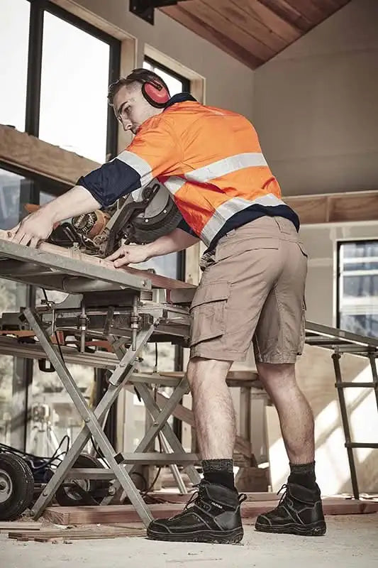 Construction worker using a chop saw wearing SYZMIK Streetworx Curved Cargo Shorts for men
