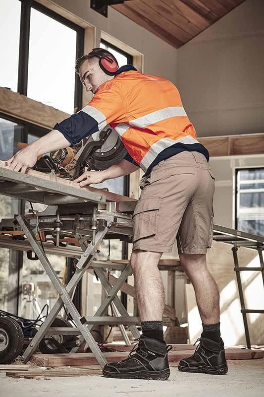 Construction worker using a chop saw wearing SYZMIK Streetworx Curved Cargo Shorts for men