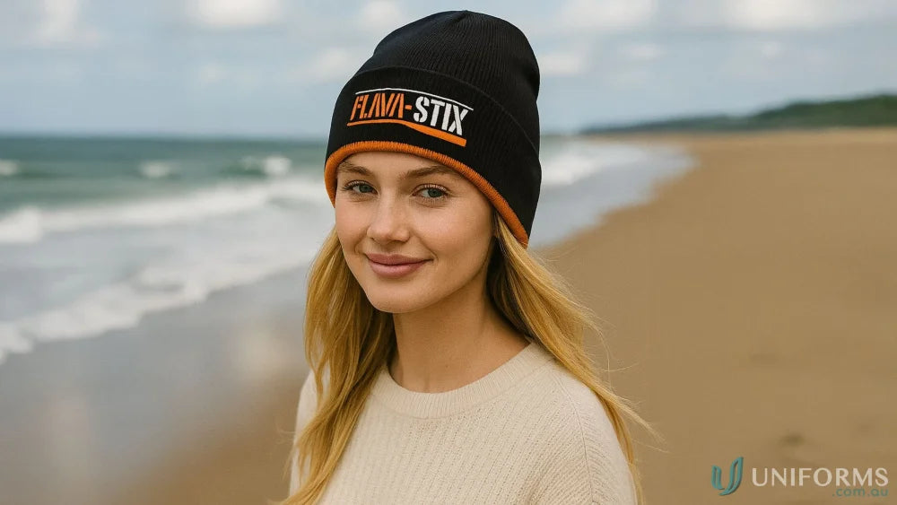 Young woman wearing a black cable knit beanie with orange trim and light sweater
