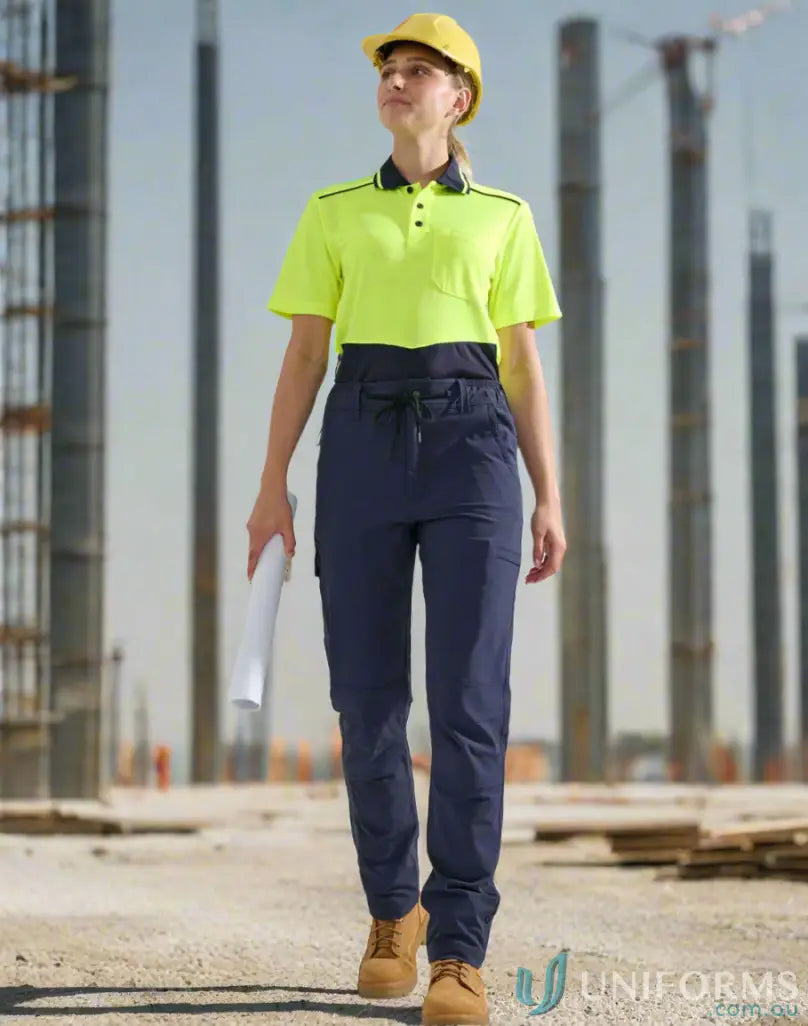 Woman in yellow hard hat and water repellent flexi work pants holding blueprint