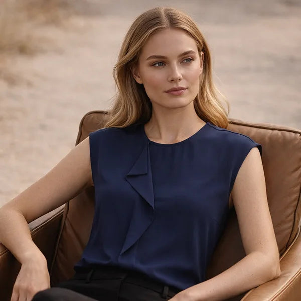 Woman wearing a navy blue sleeveless top sitting in a brown leather chair.