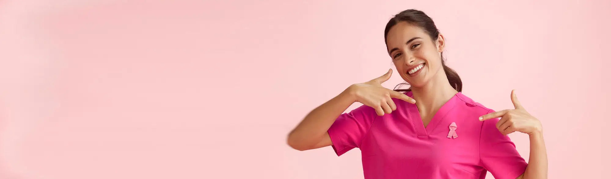 Smiling woman in pink RNF scrubs uniform with pink ribbon pin from NBCF Scrubs collection