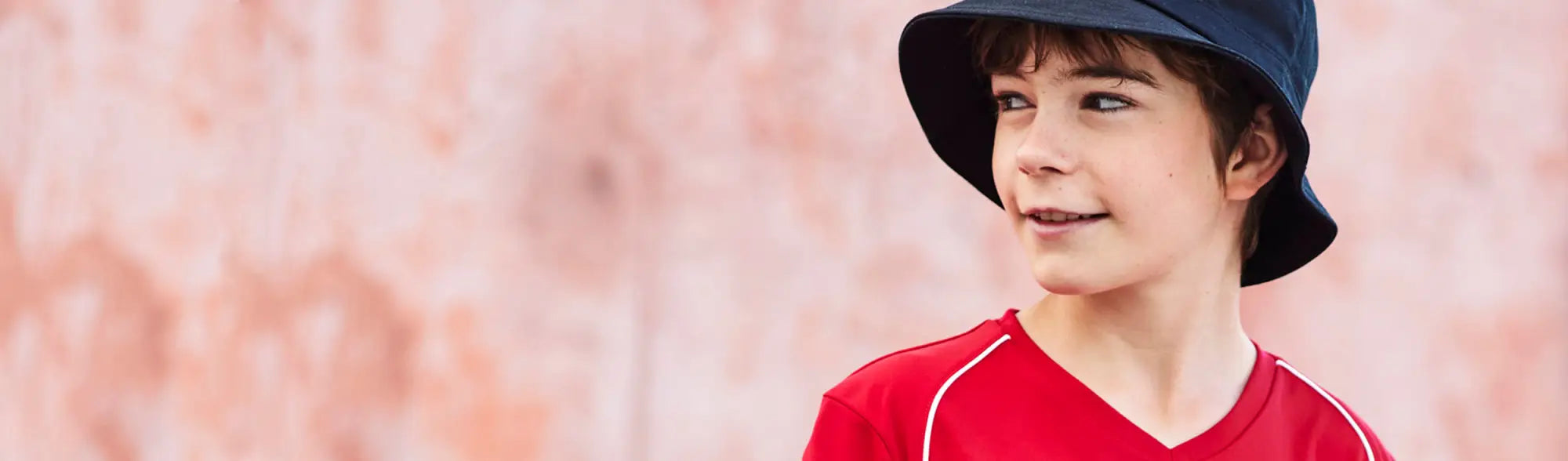 Boy in red shirt and blue hat wearing school uniforms from the School Tees collection