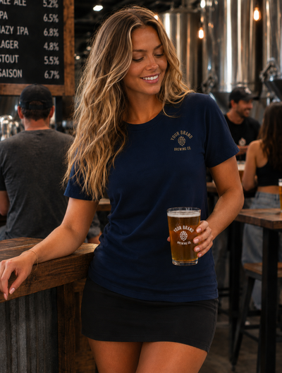 A woman in a navy blue t-shirt with a gold 'High Brand Brewing Co.' logo stands in a bar holding a glass of beer.