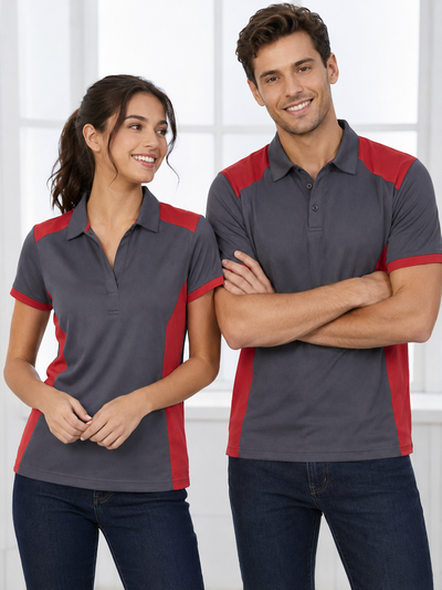 A man and a woman modeling matching short-sleeve polo shirts with a dark gray body and red side panels and sleeve trim, set against a bright white indoor background.