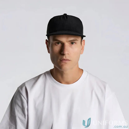 Man wearing black flat peak AS Colour Class Cord Trucker Cap in cotton 16-wale partridge