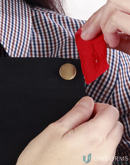 Person attaching red fabric to black Brunswick Bib Apron, stylish functional workwear