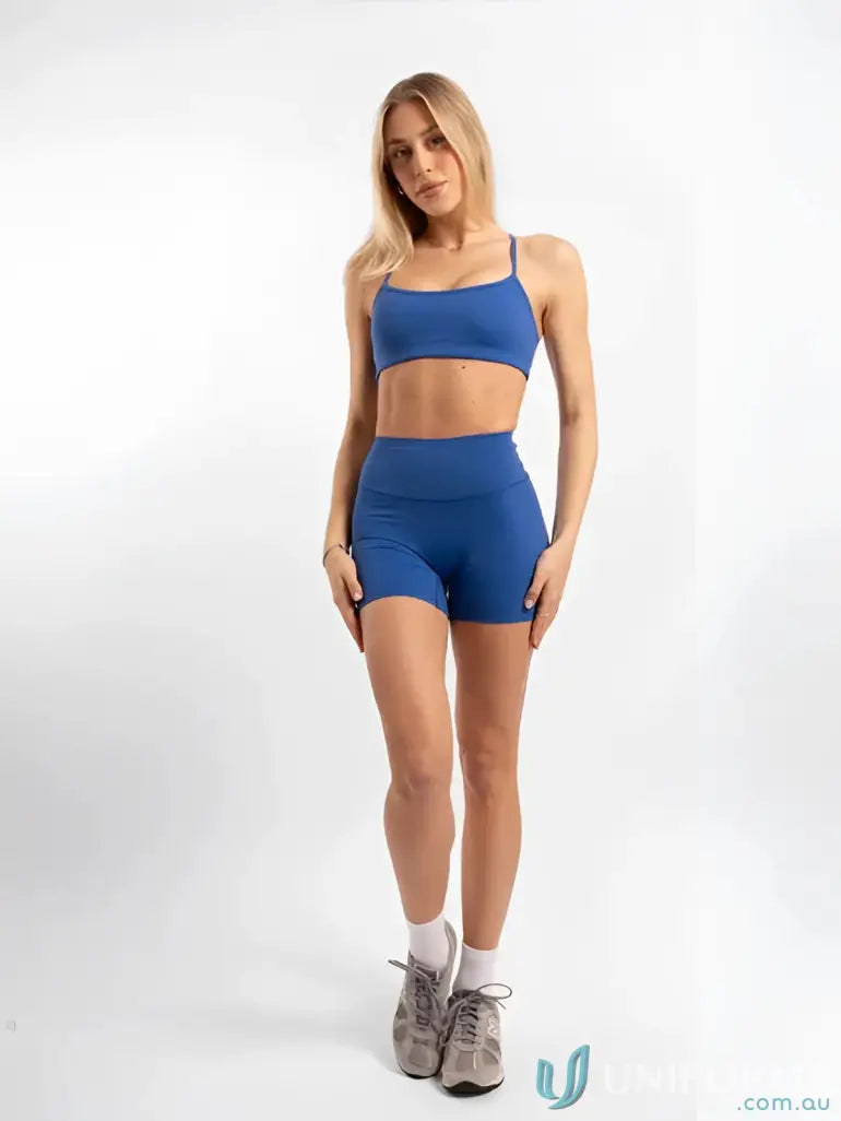 Woman in blue athletic wear showcasing Invicible Scrunch Riviera Shorts for workout uniforms