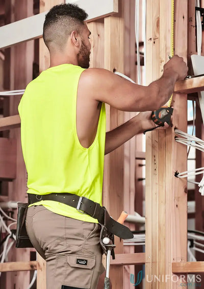 Man in neon yellow vis sleeveless tee measuring wood beam in work pants and tool belt