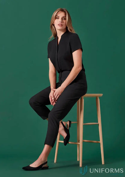 Women’s Renew mid-waist slim black jumpsuit with recycled polyester, seated on a wooden stool