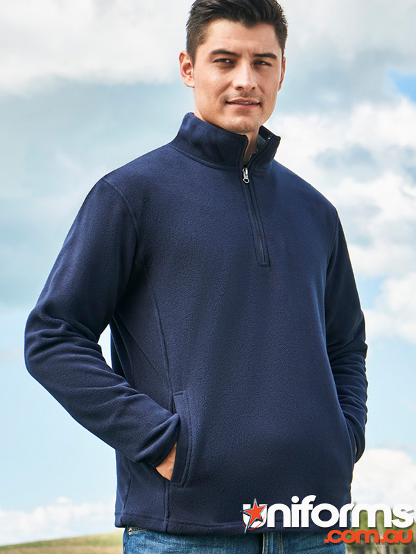 A man in a blue sweater stands in front of a lush green field, showcasing the Biz Collection Trinity Half Zip Jacket F10510.