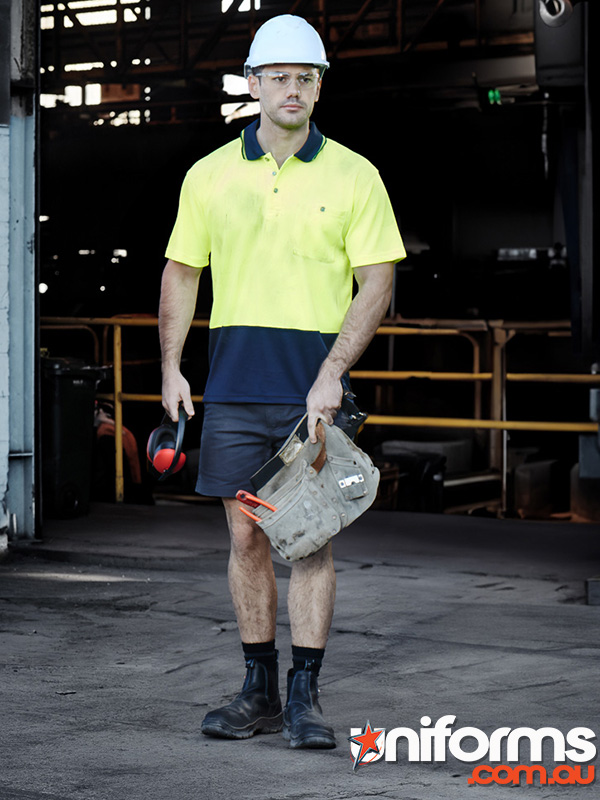 A man in a hard hat and safety vest holds a tool, wearing a Syzmic Hi Vis Basic Short Sleeve Polo ZH231.