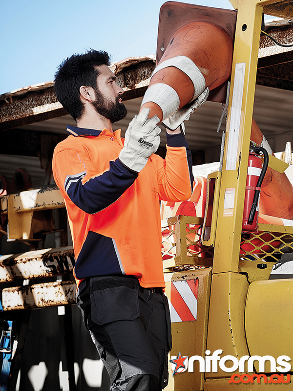 A man wearing a Syzmik Hi Vis Squad Long Sleeve Polo ZH238 stands next to a large truck, emphasizing safety attire.