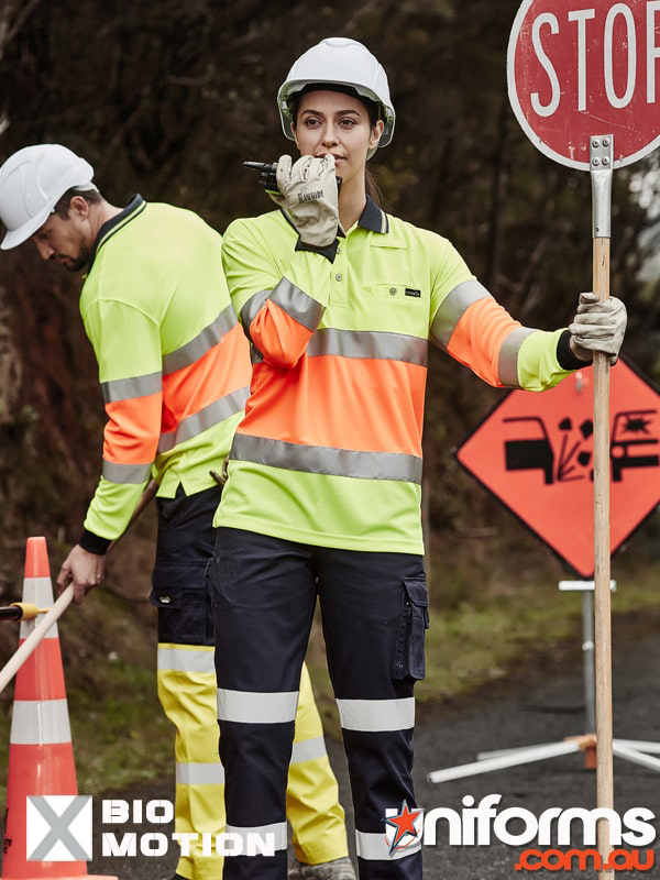 Two individuals in safety vests pose by a stop sign, highlighting the Syzmic Unisex Hi Vis Bio Motion Taped Polo ZH380.