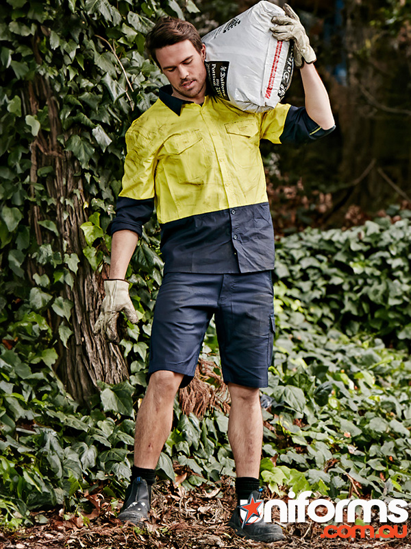 A man in a yellow and blue shirt carries a bag while wearing Syzmic brand Men's Rugged Cooling Vented Shorts ZS505.
