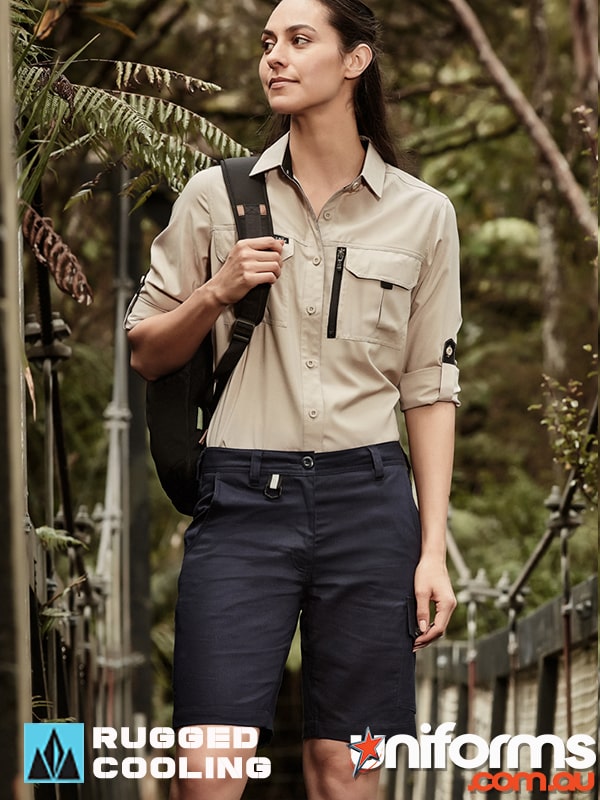 A woman in Syzmic brand rugged cooling vented shorts and a shirt stands amidst a lush green forest.