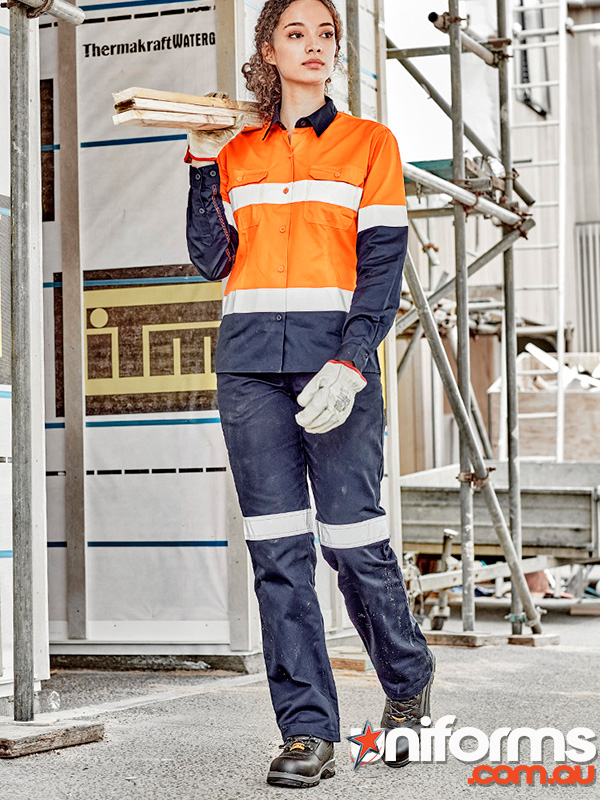 A woman in vibrant orange and blue work gear stands at a construction site, featuring the Syzmic Women's Taped Utility Pant ZWL004.