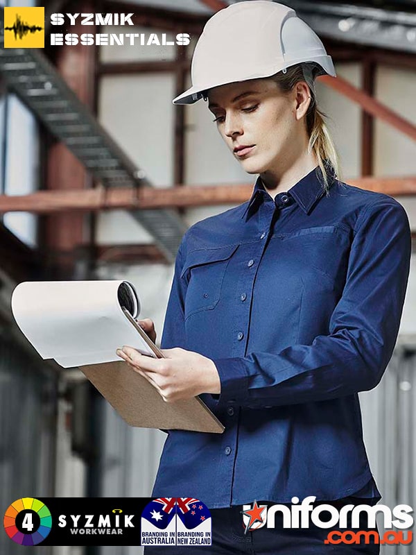 A woman in a hard hat and blue Syzmic lightweight tradie shirt stands ready for work.