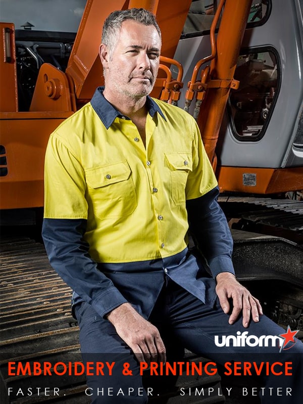 A man wearing a yellow Syzmic long sleeve shirt sits confidently on a tractor, showcasing industrial workwear.
